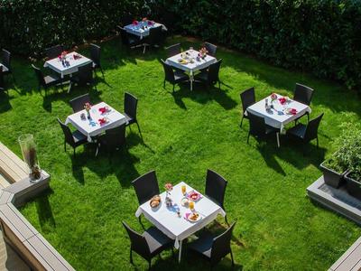 Garten mit grünem Rasen, mehreren quadratischen Tischen und schwarzen Stühlen, sonnig und gepflegt.