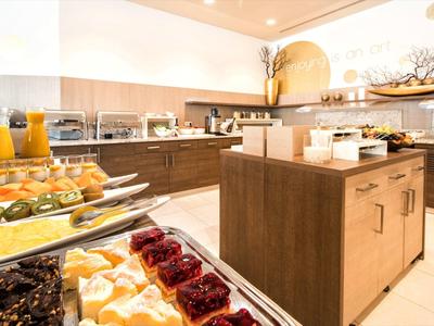 Moderne Hotelküche mit Buffet, Holzschränken, Orangensaft und verschiedenen Desserts.