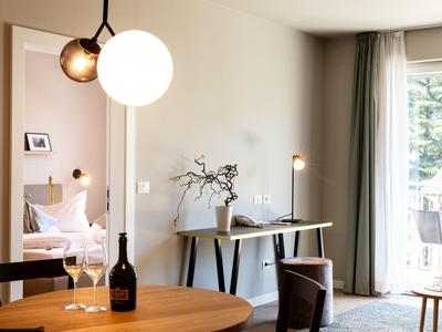 Gemütlicher Wohnbereich mit modernem Tisch, Stühlen, großen Fenstern und hellen Wänden.