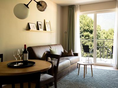 Gemütliches Wohnzimmer mit braunem Ledersofa, kleinem Holztisch und Balkon mit Grünblick.