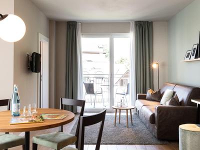 Helles Wohnzimmer mit grauem Sofa, runden Holztisch und Balkon hinter großen Fenstern.