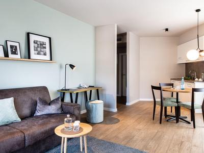 Moderner Wohn- und Essbereich mit grauem Sofa, Holzfußboden, kleinem Esstisch und hellen Wänden.