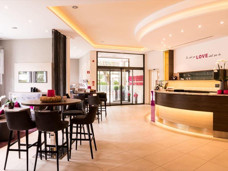 Helle Hotel-Lobby mit Holzmöbeln, Theke, Sitzgruppen und modernen Beleuchtungselementen.