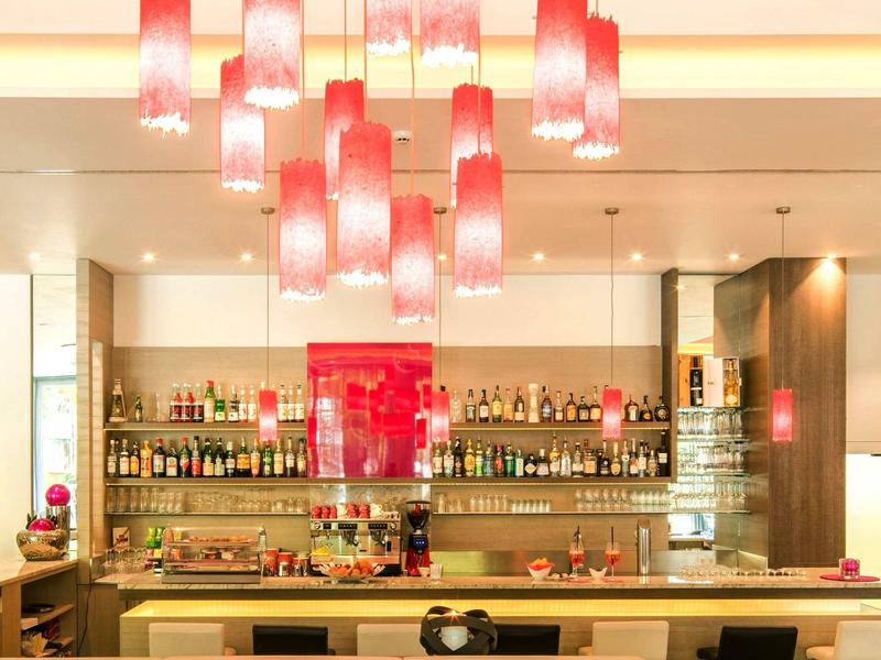 Moderner Barbereich mit hellroten Hängelampen, großem Regal voller Flaschen und hellem Tresen.