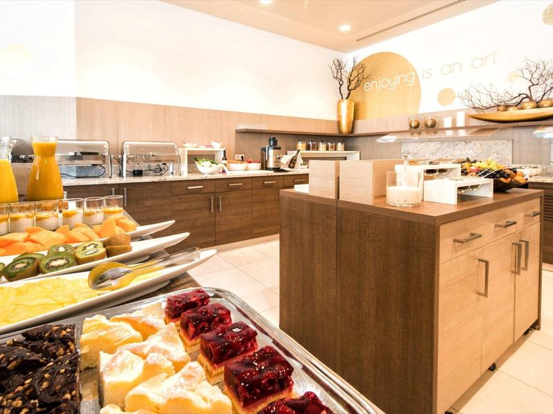 Moderne Hotelküche mit Buffet, Holzschränken, Orangensaft und verschiedenen Desserts.