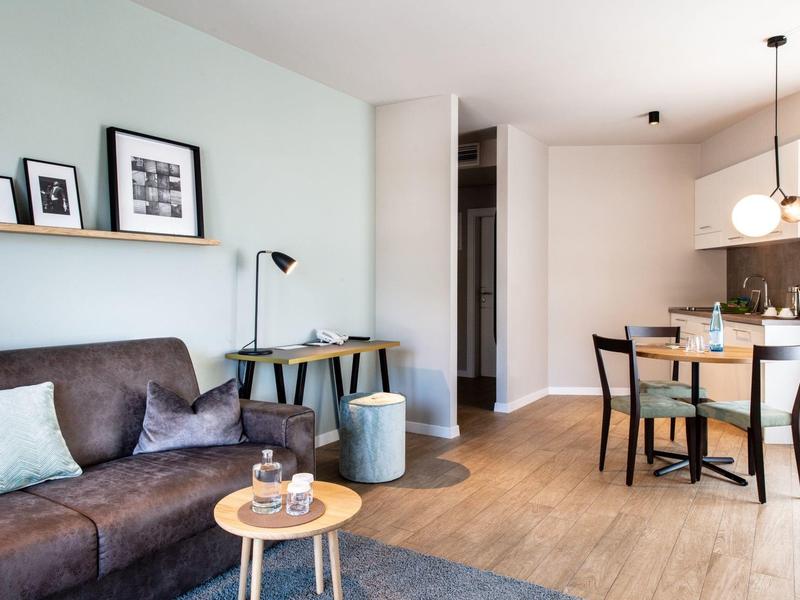 Moderner Wohn- und Essbereich mit grauem Sofa, Holzfußboden, kleinem Esstisch und hellen Wänden.