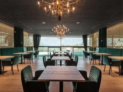 Modernes Restaurant mit Holztischen, grünen Sitzbänken und großen Fenstern.