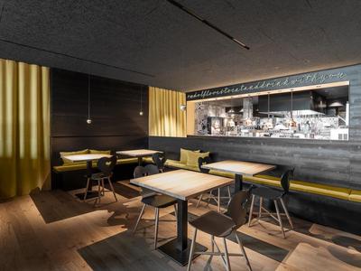 Moderner Hotel- oder Restaurantbereich mit Tischen, Stühlen und gelben Akzenten.