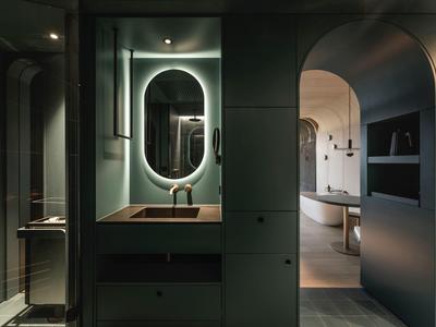 Modernes Badezimmer mit beleuchtetem Spiegel, Waschbecken und Badewanne in dunklen Tönen.