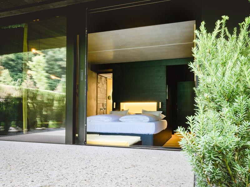 Moderner Hotelbalkon mit Blick auf ein gemütliches Bett und grüne Pflanze im Vordergrund.