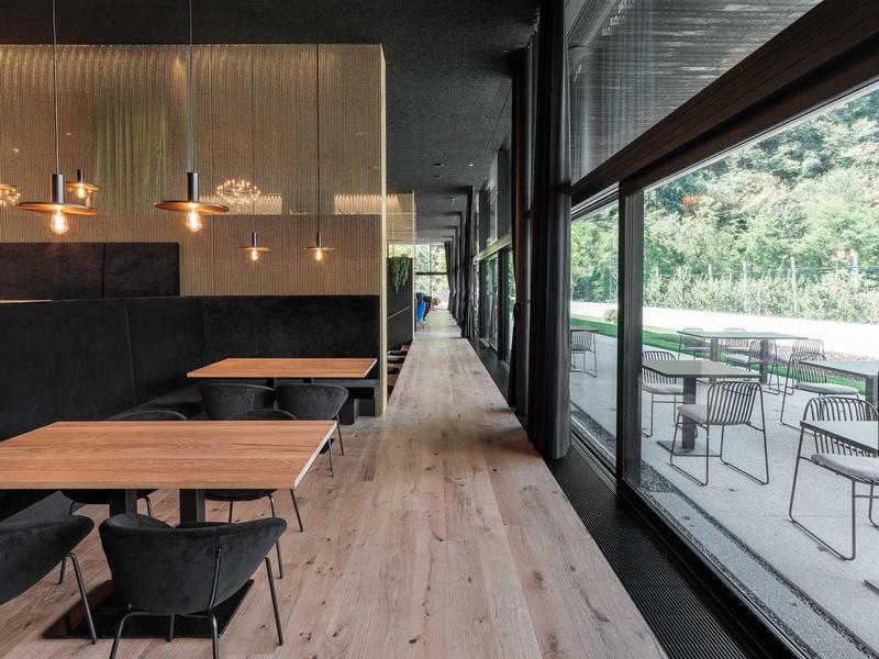 Moderner Essbereich mit Holztischen, schwarzen Stühlen und großen Fenstern zum Außenbereich.