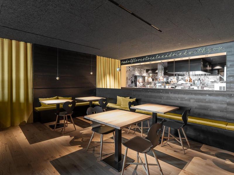 Moderner Hotel- oder Restaurantbereich mit Tischen, Stühlen und gelben Akzenten.