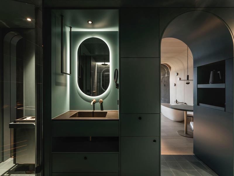 Modernes Badezimmer mit beleuchtetem Spiegel, Waschbecken und Badewanne in dunklen Tönen.