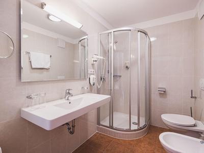 Helles Badezimmer mit Runddusche, Wandspiegel, Wandhandtuchhalter und weißen Sanitäranlagen.