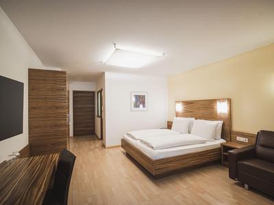 Helles Hotelzimmer mit Doppelbett, braunem Sofa, Holzfußboden und Fernseher an der Wand.