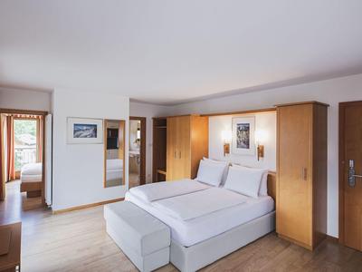 Helles Schlafzimmer mit Doppelbett, Holzschränken, Fenstern und warmen Holz- und weißen Farben.