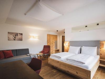 Gemütliches Schlafzimmer mit Holzbett, Sofa, Stuhl und warmem Licht in natürlicher Farben.