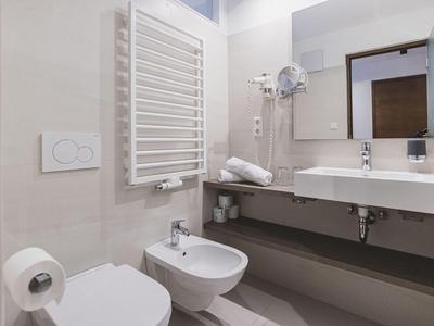 Helles Badezimmer mit Toilette, Bidet, Waschbecken, Handtuchheizung und Wandspiegel.