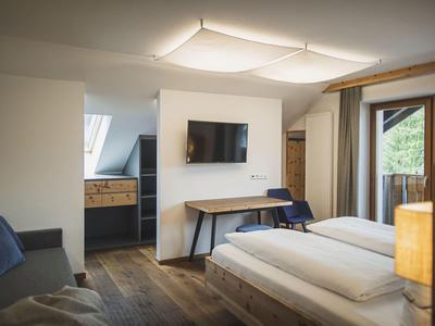 Modernes Hotelzimmer mit Holzfußboden, Doppelbett, Sofa, Fernseher und Balkon mit Blick ins Grüne.