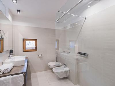 Moderne, helle Badezimmer mit bodengleicher Dusche, Wand-WC und Bidet, weißen Fliesen und Holzfenster.