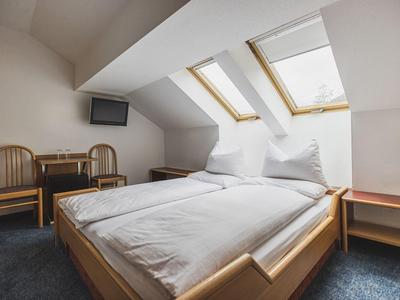 Schlichtes Schlafzimmer mit Doppelbett, weißen Bettdecken, zwei Holzstühlen und Dachfenstern.