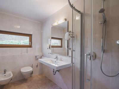 Helles Bad mit weißem Waschbecken, Bidet, Toilette, Duschkabine und kleinem Fenster an der Wand.