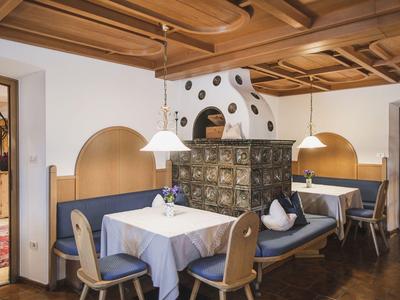 Gemütlicher Gastraum mit Holzbalkendecke, blauer Polsterbank, Keramikofen und gedeckten Tischen.