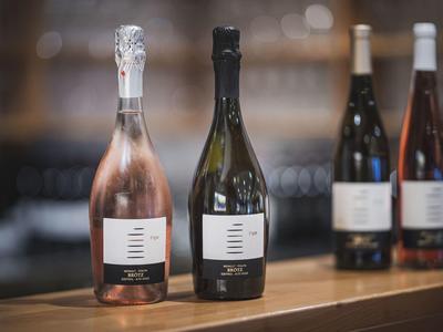 Vier Weinflaschen, zwei vorne mit rosa und dunkelgrünem Glas, zwei hinten unscharf stehend.