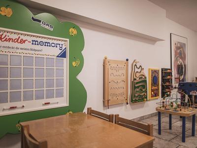 Kinderspielzimmer mit buntem Memory-Spielbrett, Wandelementen und Holztischen mit Stühlen.