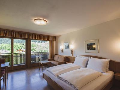 Helles Hotelzimmer mit Doppelbett, Balkon und Blick auf grüne Berge.