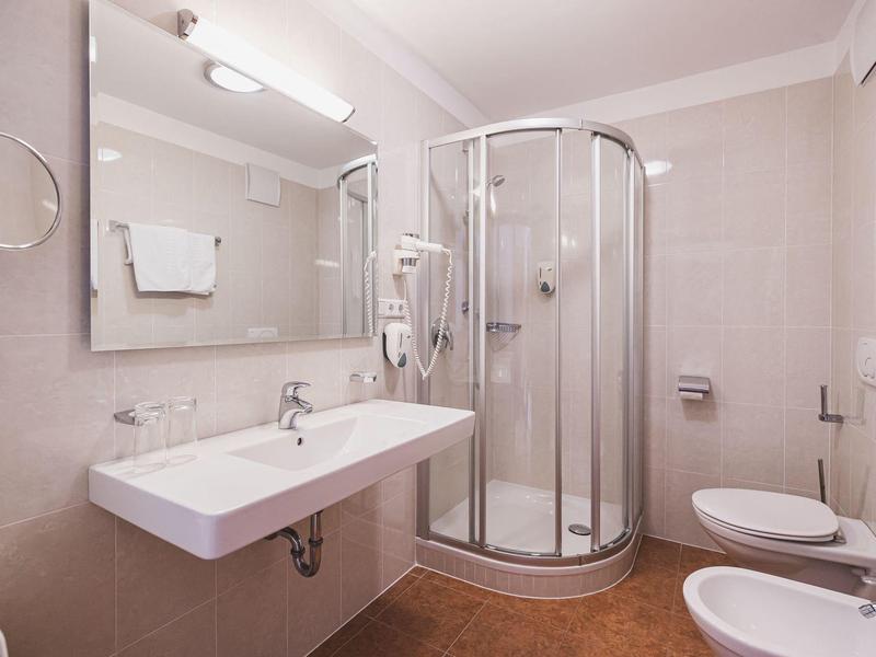 Helles Badezimmer mit Runddusche, Wandspiegel, Wandhandtuchhalter und weißen Sanitäranlagen.