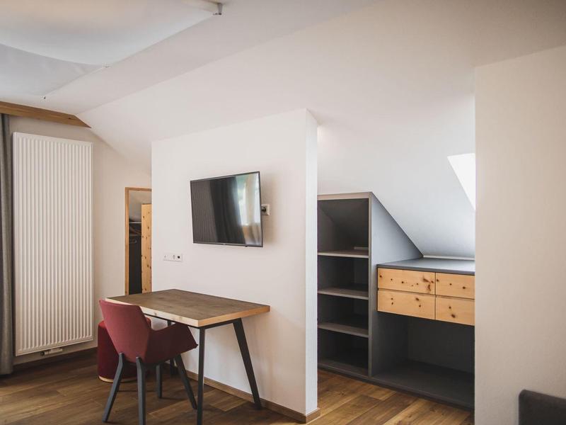 Moderner Raum mit Holzboden, kleinem Schreibtisch, rotem Stuhl, Wand-TV und Regal mit Schubladen.