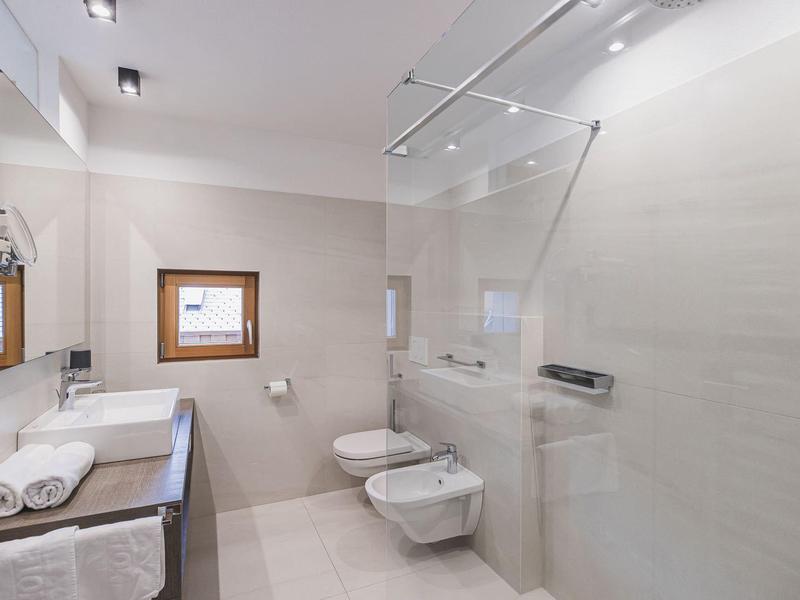Moderne, helle Badezimmer mit bodengleicher Dusche, Wand-WC und Bidet, weißen Fliesen und Holzfenster.