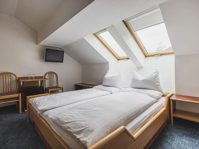 Schlichtes Schlafzimmer mit Doppelbett, weißen Bettdecken, zwei Holzstühlen und Dachfenstern.