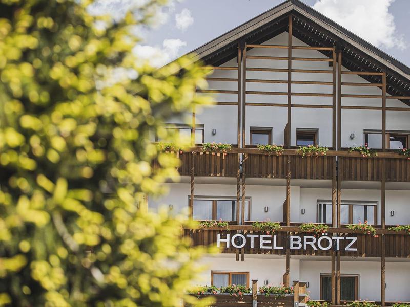 Fassadenansicht eines traditionellen Hotels mit Holzbalkonen und grünen Pflanzen im Vordergrund.