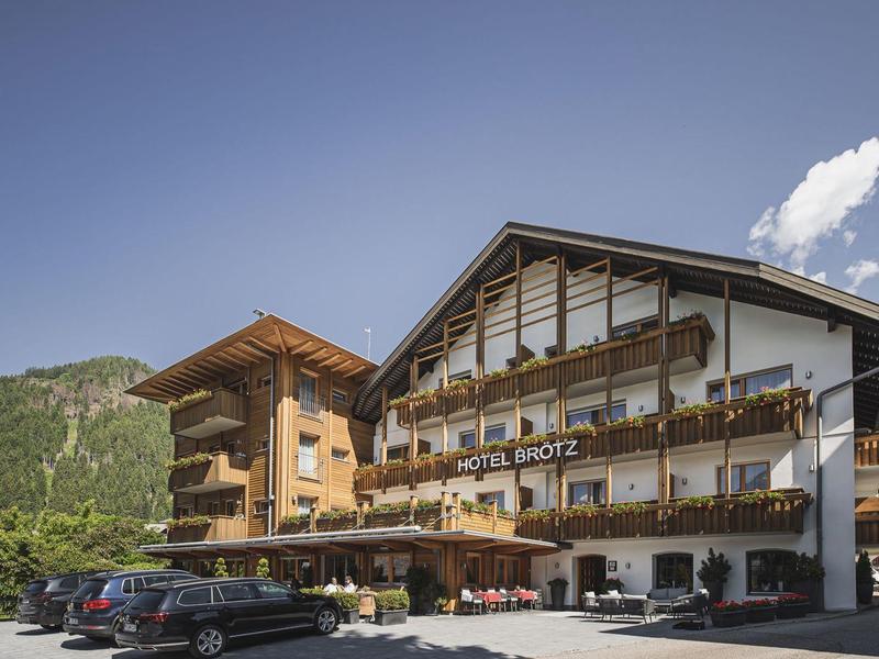 Ein großes Hotelgebäude mit Holzbalkonen, Blumendekor und Bergen im Hintergrund unter blauem Himmel.