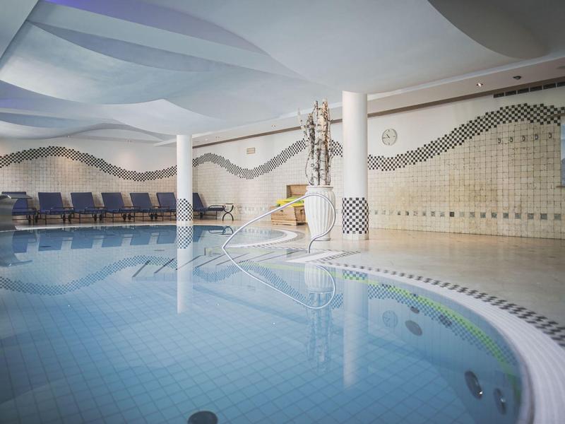 Innenbereich eines Schwimmbads mit blauen Fliesen und wellenförmigen Wandmustern.