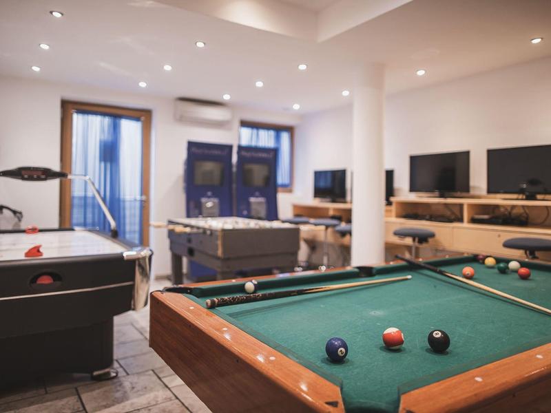 Ein Spielzimmer mit Billardtisch, Airhockey, Tischkicker und mehreren Fernsehern an der Wand.