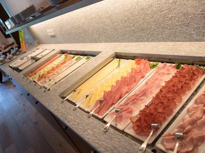 Buffet mit verschiedenen fein geschnittenen Wurst- und Käsesorten in rechteckigen weißen Schalen.