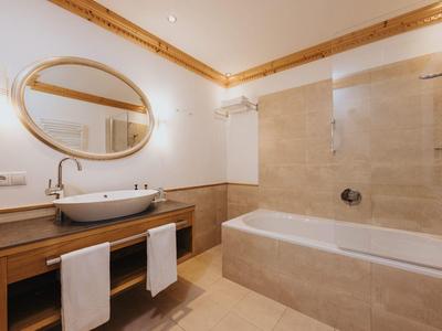 Helles Badezimmer mit Holzdecke, ovalem Spiegel, Waschbecken auf Holzunterschrank und Badewanne.