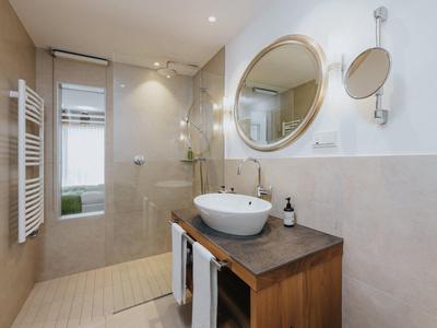 Moderner, heller Badraum mit Holzwaschtisch, rundem Spiegel und offener Dusche mit Glaswand.