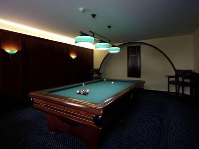 Ein dunkler Billardraum mit grünem Tisch, Kugeln und moderner Beleuchtung.
