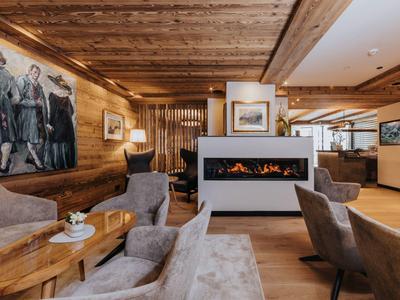 Gemütliches Wohnzimmer mit Holzdecken, Kamin, grauen Sesseln und einem großen Gemälde an der Wand.