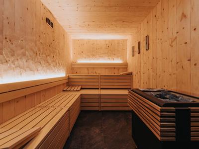 Innenraum einer Sauna mit hellen Holzplatten, Holzbänken und Heizgerät rechts vorne.