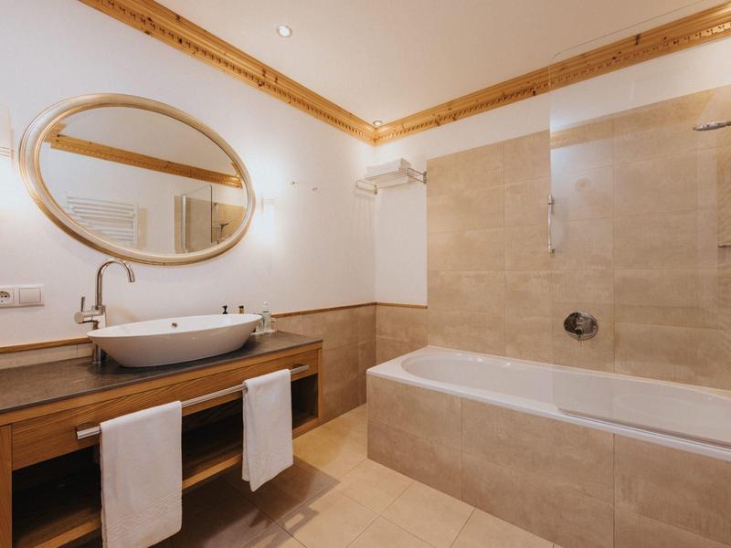 Helles Badezimmer mit Holzdecke, ovalem Spiegel, Waschbecken auf Holzunterschrank und Badewanne.