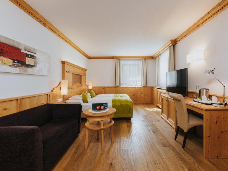 Modern eingerichtetes Hotelzimmer mit Holzmöbeln, Sofa, Bett, Schreibtisch und Fernseher.