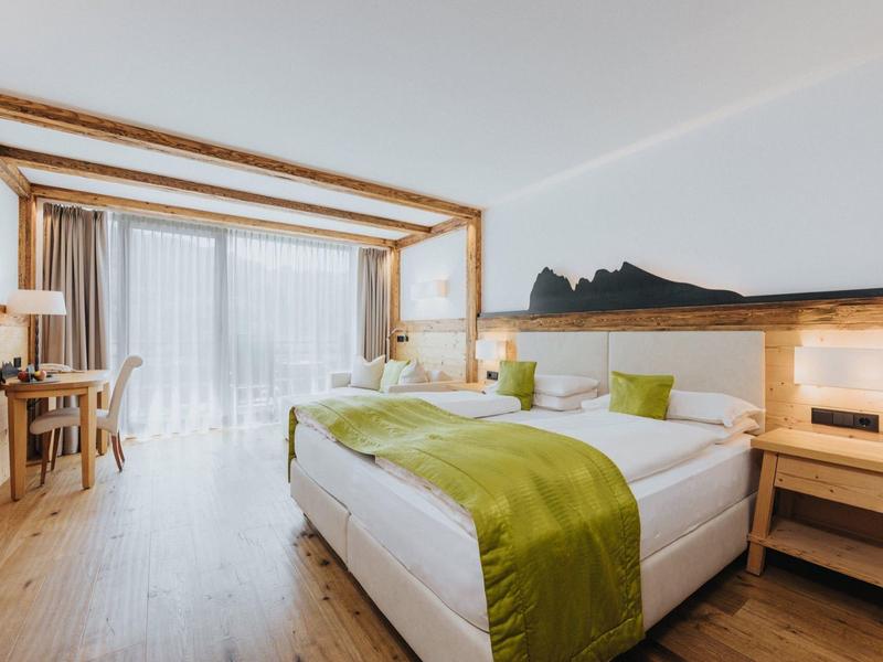 Hell eingerichtetes Schlafzimmer mit großem Bett, Holzmöbeln und bodentiefen Fenstern.