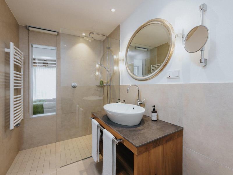 Moderner, heller Badraum mit Holzwaschtisch, rundem Spiegel und offener Dusche mit Glaswand.