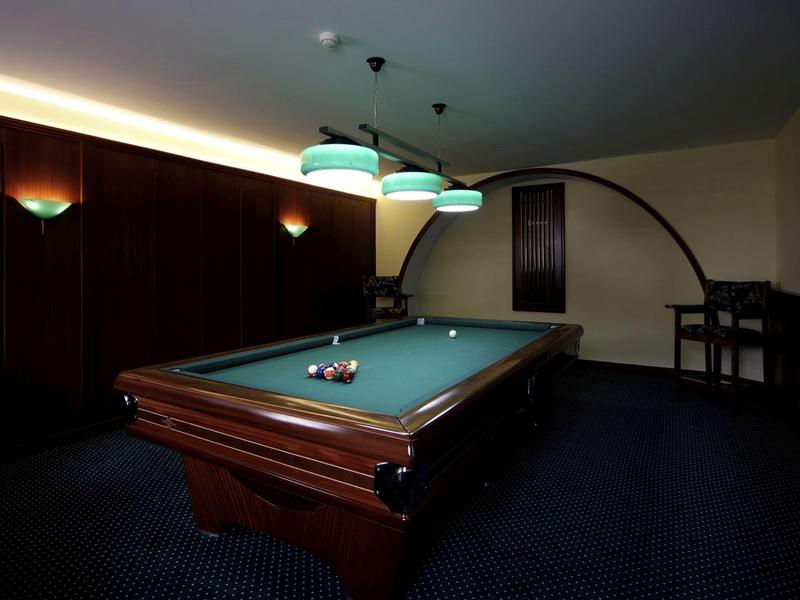 Dunkler Raum mit einem Billardtisch, drei Hängelampen und hochstuhl an der Wand.