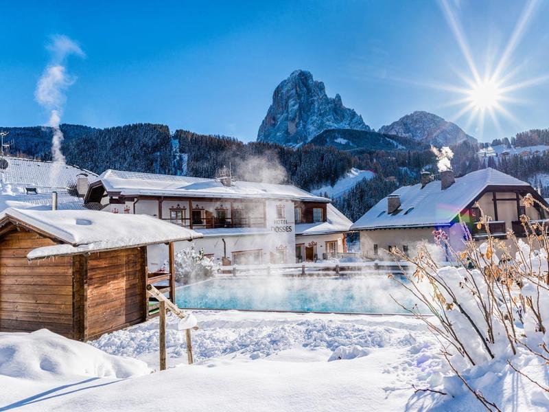 Freiluftpool mit Dampfschwaden umgeben von Schnee und Bergen bei Sonnenschein